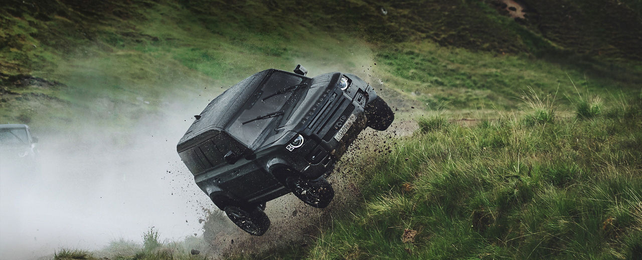 Range Rover Defender jumping in the air, driving on a hilly terrain