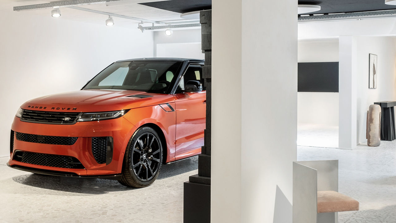 An orange Range Rover pictured from the front in a white exhibition space.