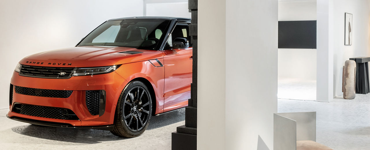 An orange Range Rover pictured from the front in a white exhibition space.
