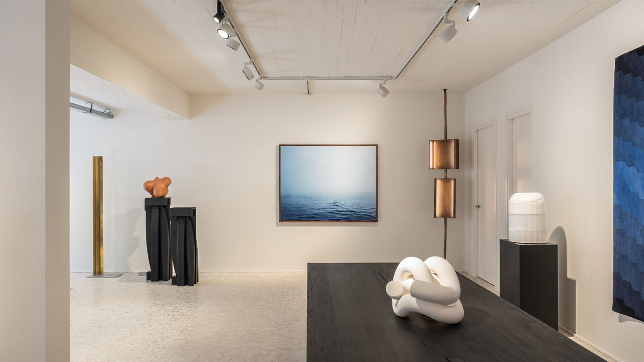 A view of an exhibition room with a blue painting and modern statues on dark stand.