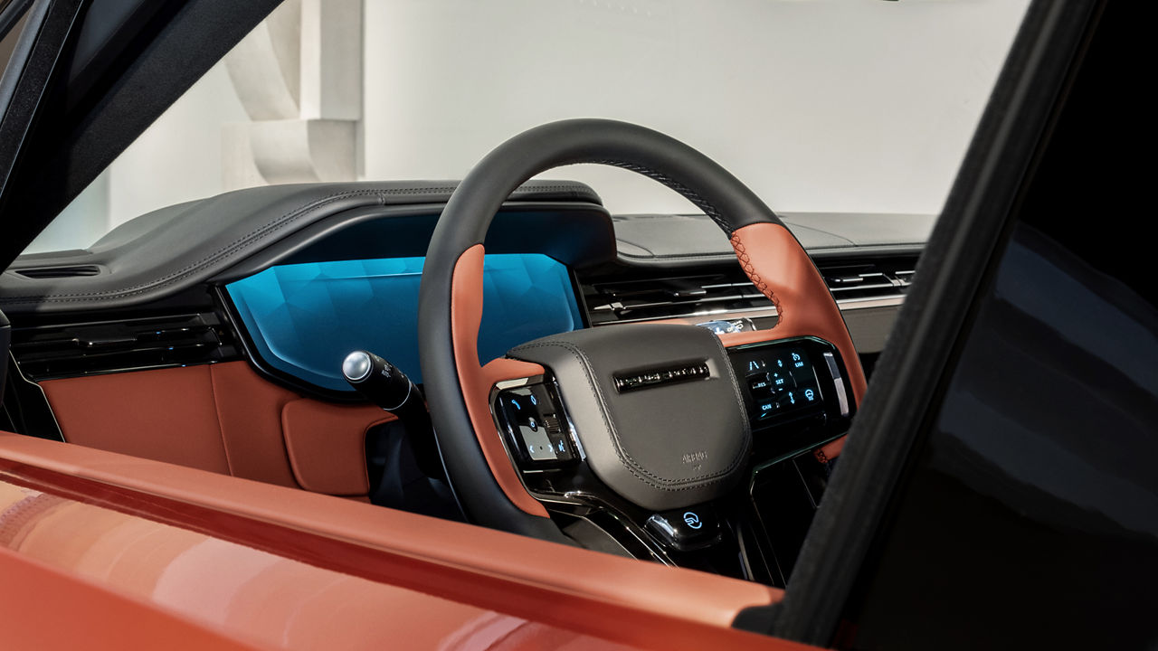 A view from outside to the interior of an orange Range Rover where the wheel can be seen.