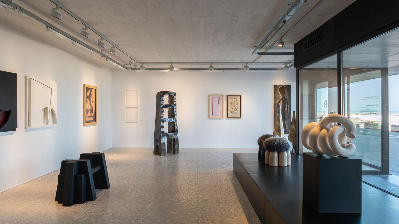 A view of a exhibition room with statues and art on a white wall.