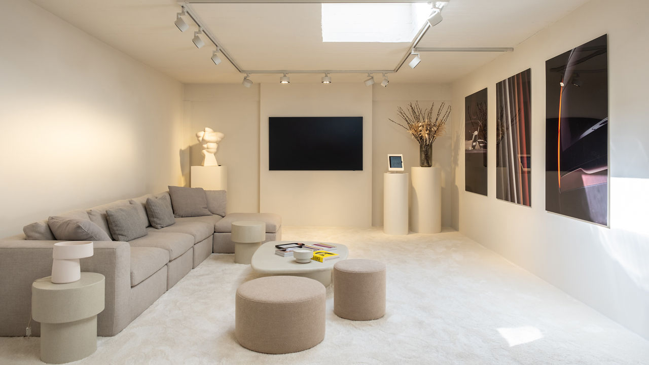 Room with a beige sofa, coffee tables and a wall TV and three dark-shade posters hanging on the wall.