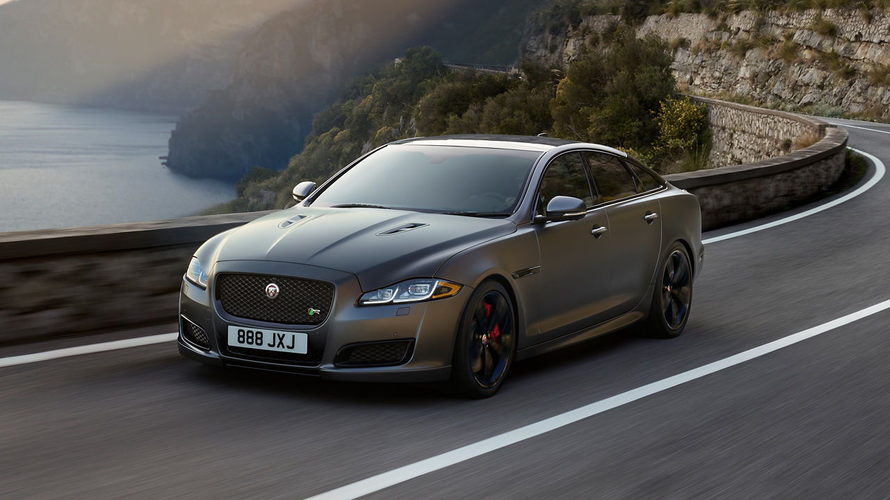 Jaguar XJ running on road surrounded with mountains and river