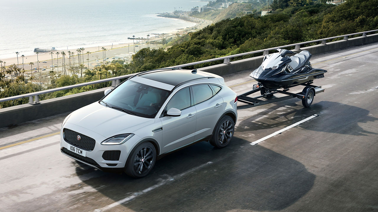 Jaguar E-PACE towing jet ski parked on bridge near beach area