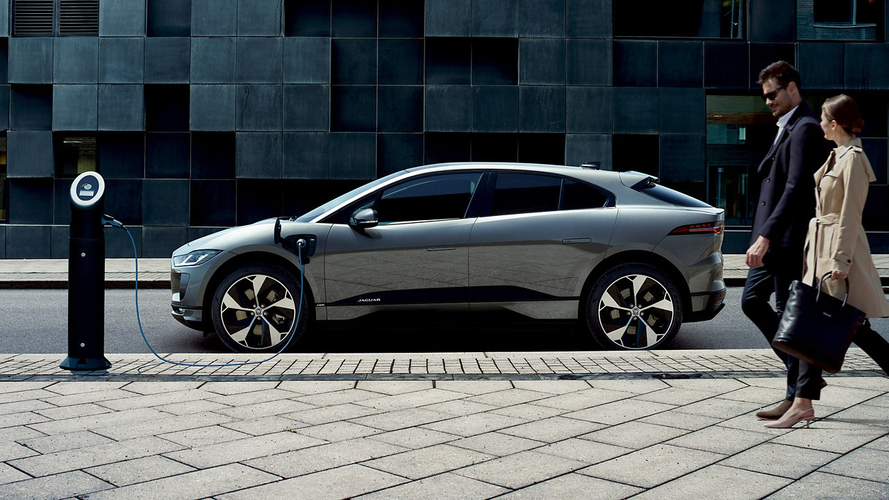 Jaguar I-PACE parked at Charging Station and Two Couple Walking on Street Road