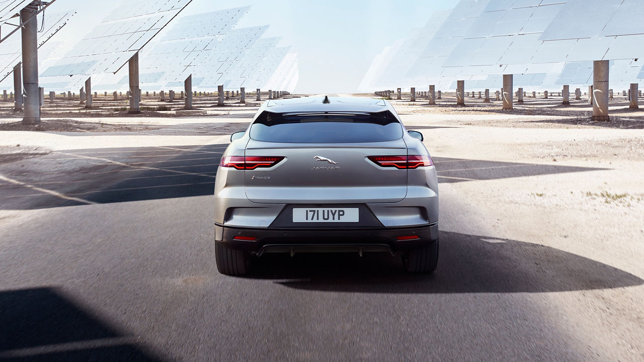Jaguar I-PACE moving on sand road surrounded by solar pannels